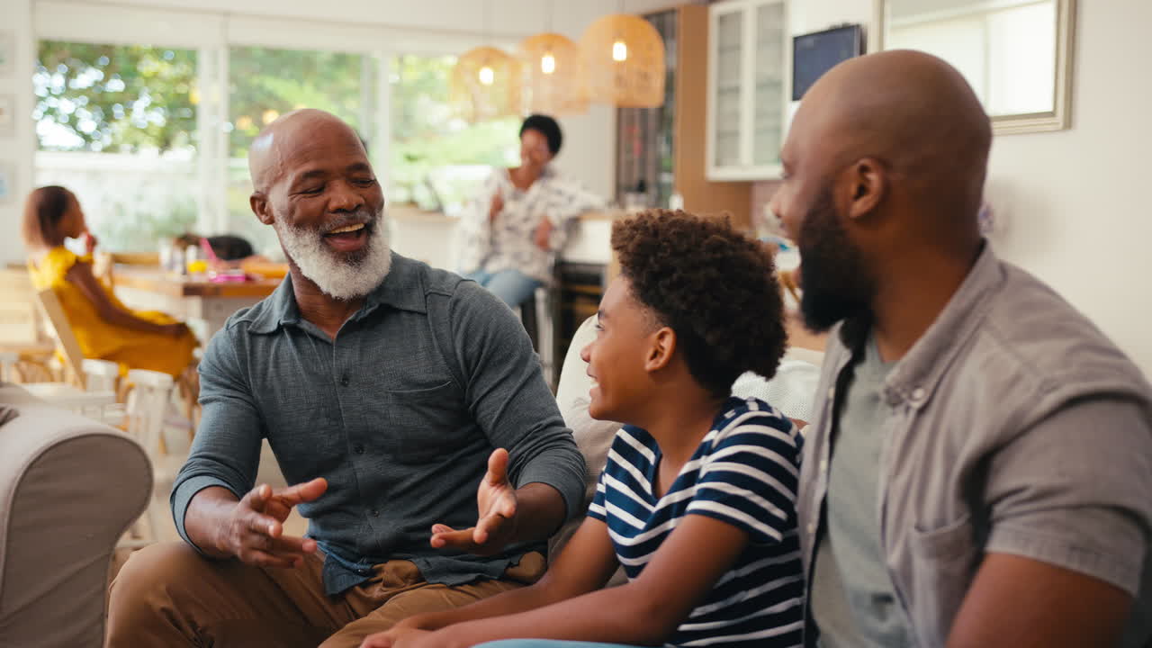 Laughing Multi-Generation Male Family Hanging Out On Sofa At Home Talking Together