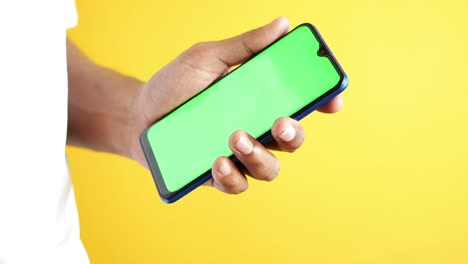 mano sosteniendo un teléfono inteligente con una pantalla verde contra un fondo amarillo