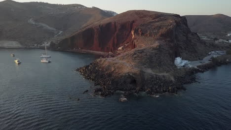 Low-aerial-orbits-Santorini's-Red-Beach-cliffs-to-St-Nicholas-church