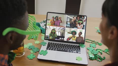 Smiling-diverse-group-of-friends-with-beer-wearing-clover-shape-items-on-video-call-on-laptop