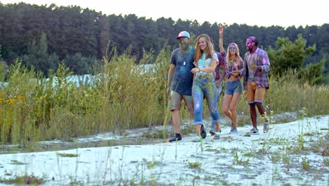 compañía de jóvenes y alegres amigos multiétnicos, niñas y niños, caminando al aire libre en la naturaleza y riendo durante el festival holi