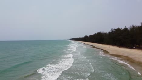 Aerial:-flying-left-to-right-with-Long-Ocean-waves,-reach-the-shore-in-Southern-Thailand