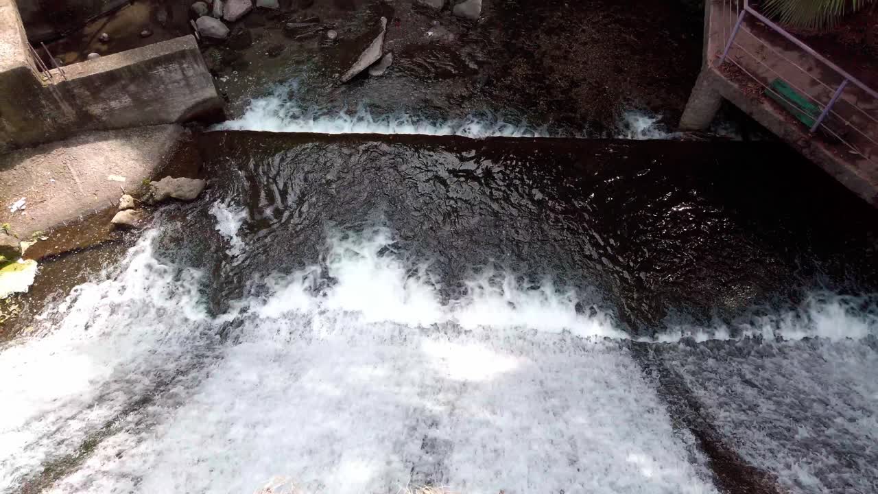 Overhead view of river flowing over a step structure with greenery and concrete walls, pan up movement in Parque Chapultepec