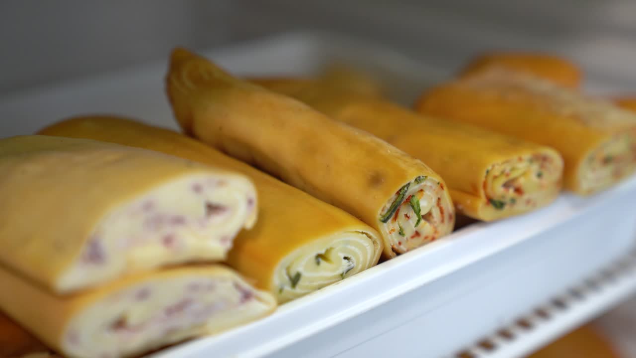Gulungan keju buatan sendiri yang lezat dengan berbagai isian, siap disajikan atau dikemas. Roulade keju gurih dalam nampan, menawarkan camilan atau hidangan pembuka segar untuk dijual.