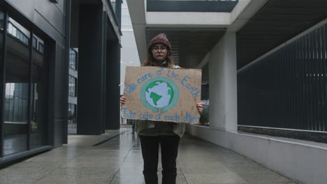 joven activista con pancarta haciendo una protesta silenciosa contra el cambio climático mientras mira la cámara