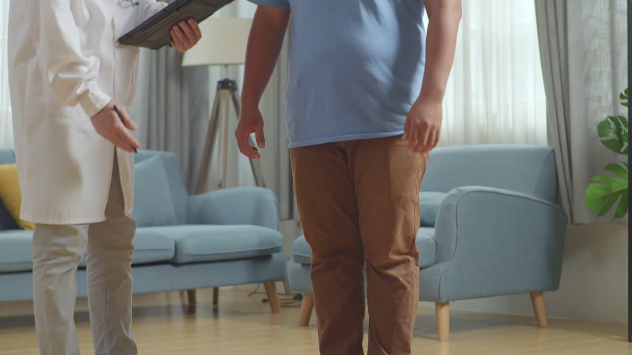 아시안 남성 의사가 클리닉에서 한 남성 환자를 가지고 있습니다. 환자는 무게를 측정하는 기계를 사용하고, 의사는 태블릿에 기록합니다.