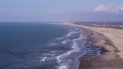 rough waves break on empty scheveningen beach with den haag backdrop - aerial