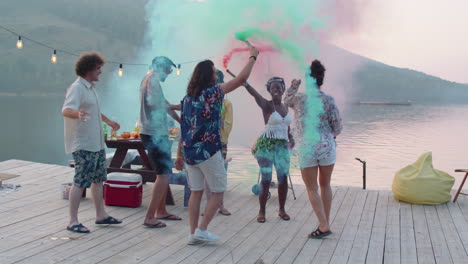 friends dancing with colored smoke bombs on lake party