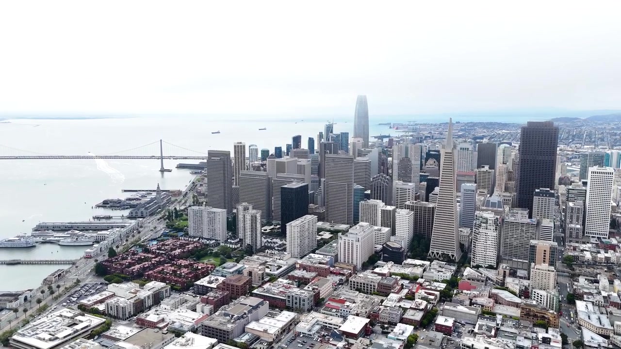 カリフォルニア州サンフランシスコのドローン空撮。ダウンタウンのスカイライン、エンバカデロのウォーターフロント、ベイブリッジ、市街地、そしてサンフランシスコ湾を映し出す。広角のシネマティックな都市の紹介映像。