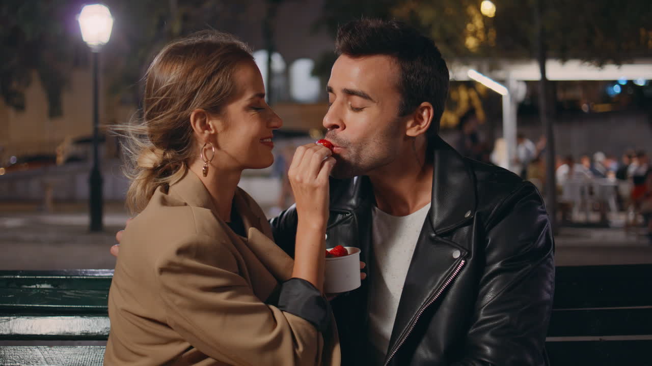 Sweethearts dating valentine evening eating strawberry on city street closeup.