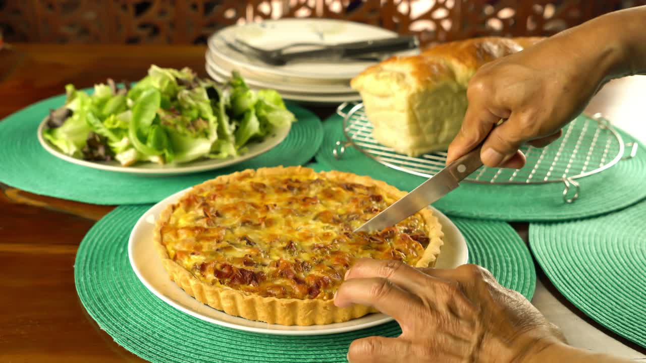 mano mayor usando un cuchillo cortando delicioso guisante verde casero y quiche de tocino.