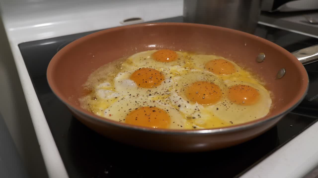 Telur mata sapi digoreng di wajan di atas kompor ditaburi bubuk lada hitam