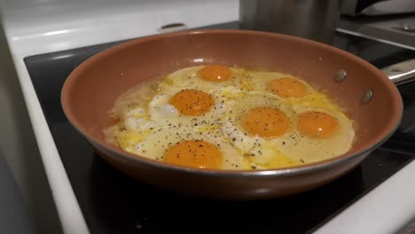 huevos al sol fritos en una sartén de estufa espolvoreados con pimienta negra en polvo