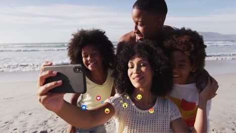 Animación-De-íconos-De-Los-Medios-Sobre-Una-Feliz-Familia-Afroamericana-Tomándose-Selfie-En-Una-Playa-Soleada