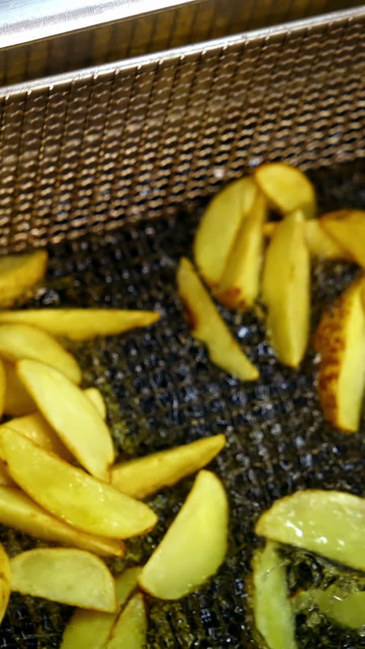Pieces of potato in deep fryer before cooking. Many bubbles appears in hot oil. Process of frying potato in boiled oil. Vertical video