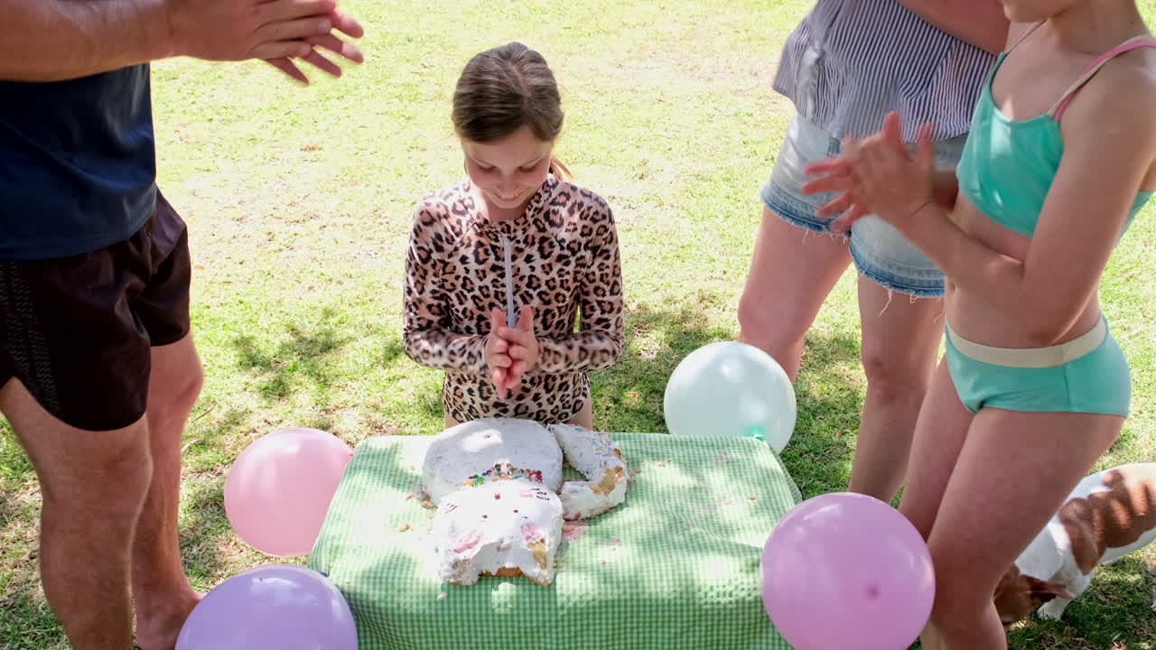 Family sings happy birthday to smiling young girl near cat-shaped cake, slomo