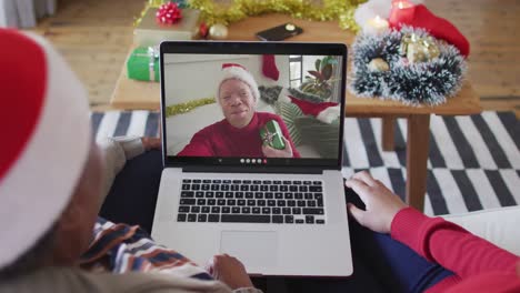 Madre-E-Hija-Afroamericanas-Usando-Una-Computadora-Portátil-Para-Una-Videollamada-Navideña-Con-Un-Hombre-En-La-Pantalla