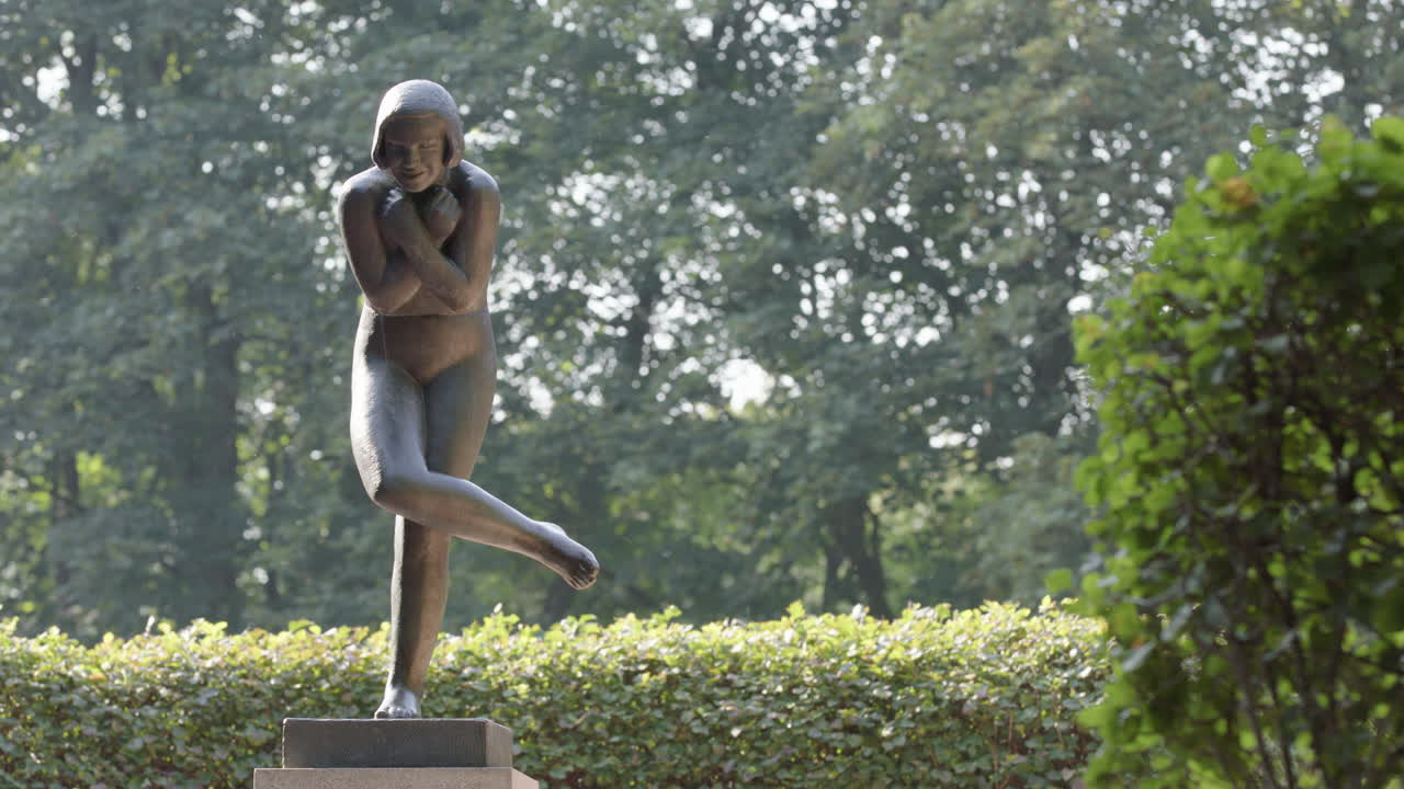 Tourist passes the woman on one leg, with crossed arms, Vigeland sculpture park
