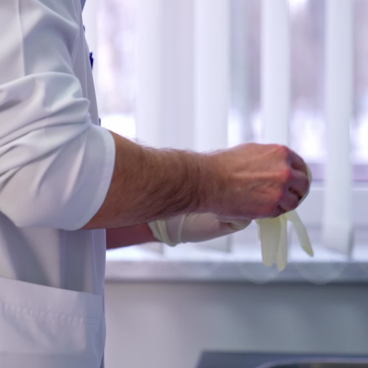 Male medic wearing white coat putting on white latex gloves. Close up. Doctor's protection at hospital work