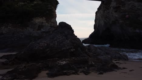 Revealing-low-left-to-right-shot-of-waves-coming-towards-the-beach-past-a-rock-during-the-morning-in-Newquay,-Cornwall,-England,-Uk