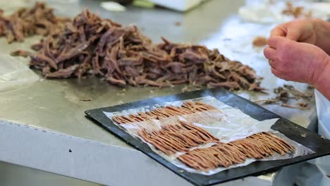 worker tears, rips, and shreds dry pieces of shellfish placing onto tray for packaging