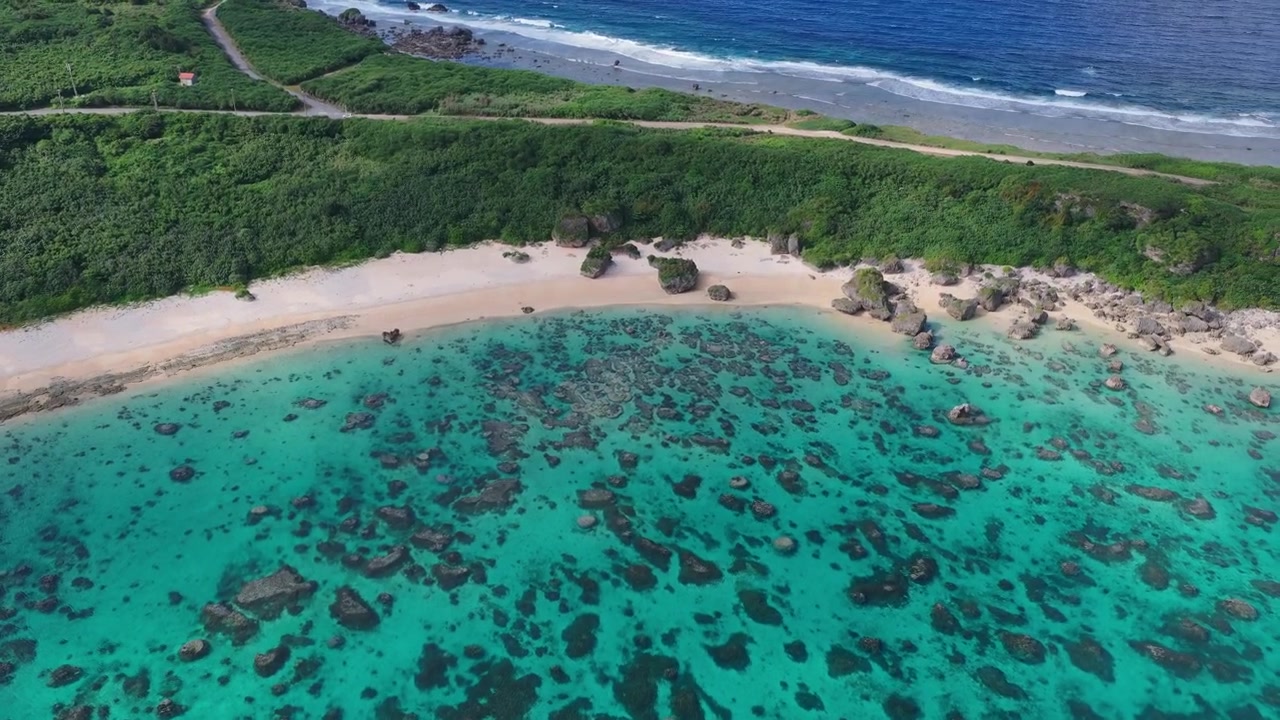 Filmato aereo orizzontale che avanza con panoramica a destra e inclinazione verso il basso sopra la barriera corallina e la costa vicino al faro di Hennasaki e alla spiaggia di Maibah, Miyakojima, Okinawa, Giappone.