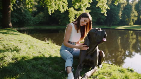 woman and her great dane relaxing by a pond in a sunny park