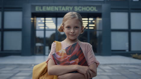 elementary age girl holding books close up. happy blonde child posing at campus.