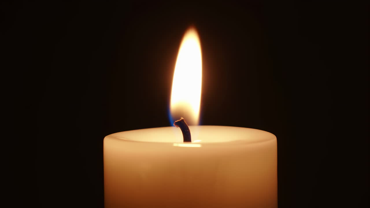 Primo piano di una fiamma di candela che brucia nell'oscurità, un solitario cero di cera emette un caldo bagliore dorato con uno stoppino dalla punta blu.