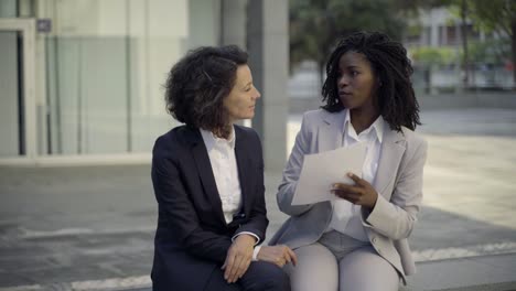 serious businesswomen sitting on street and discussing contract