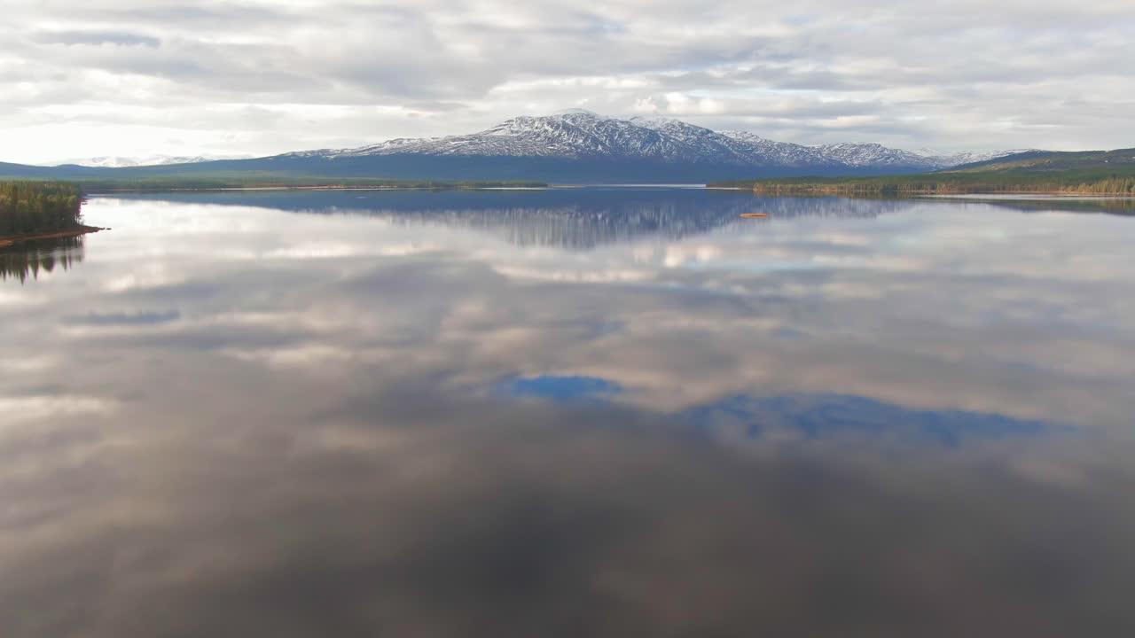 lago del bosque alpino sueco que refleja montañas nevadas