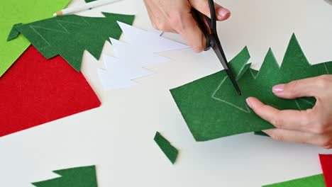 manos de mujer cortan un árbol de navidad de tela verde con tijeras usando una plantilla