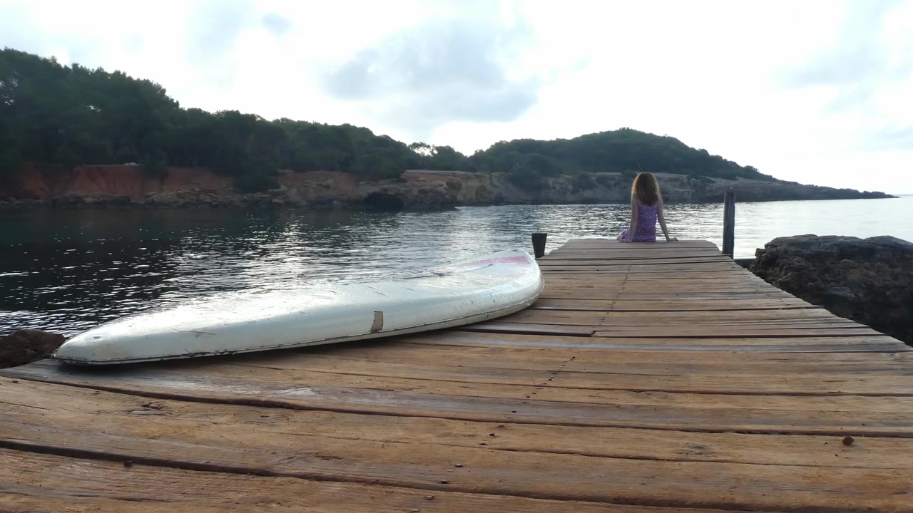Una ragazza seduta su una passerella che osserva la bellezza della costa di Ibiza al mattino