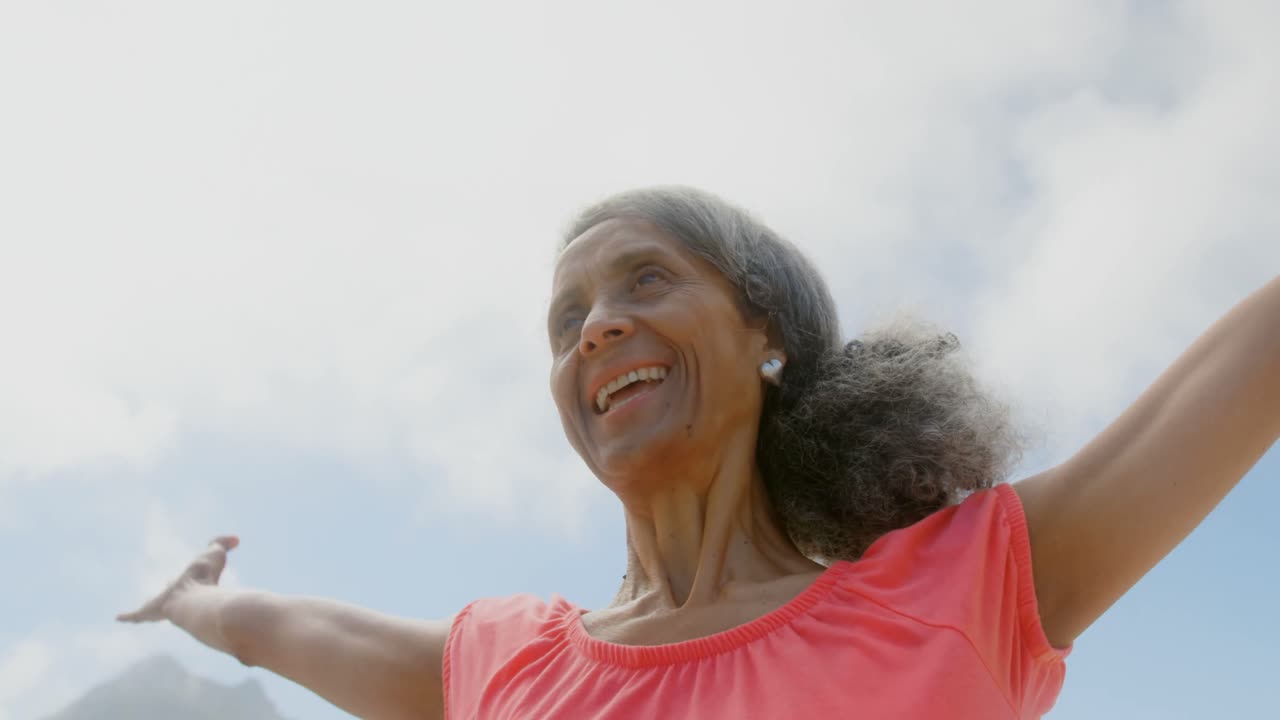 Low angle view of active senior African American woman stretching her arms in sunshine on the beach