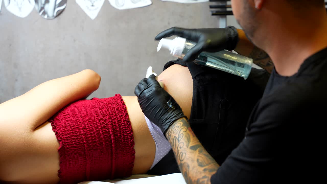 Tattoo artist creating delicate script tattoo on client's hips