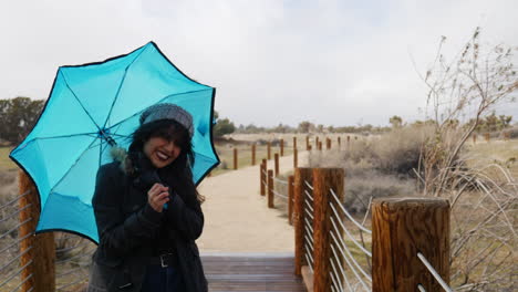 a pretty woman with a blue umbrella standing in strong wind during a rain storm and bad weather