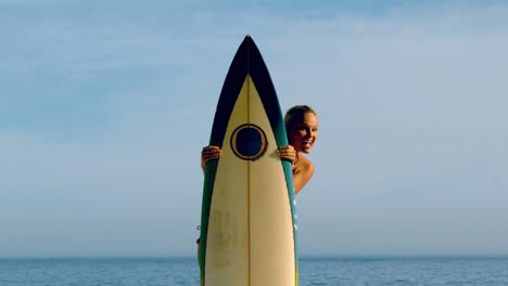 female surfer peeking out from behind her board