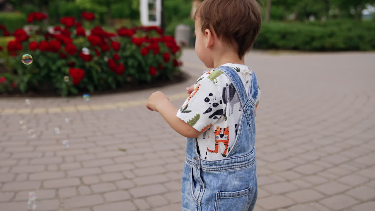 Sweet baby boy in jeans romper. Cute child playing with soap bubbles. Walk in the park.
