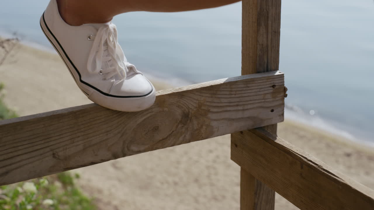Nærbillede af kvindeben i hvide sneakers foran et solrigt havlandskab.