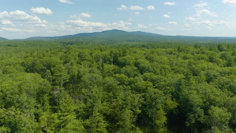 Aerial-drone-forward-moving-shot-over-the-mountain-forest-beside-sunset-lake-in-New-Hampshire,-USA