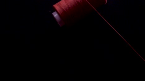 red-thread-spin-spool-on-bobbin-unroll-fall-black-bg-slow-motion-static