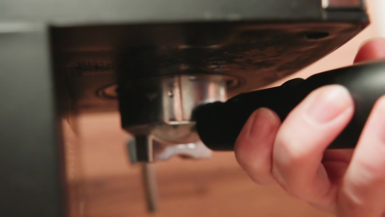 Close low angle closeup of hand locking portafilter into espresso machine group head, showing upward placement, slight wrist turn, firm grip, and careful brewing preparation before extraction