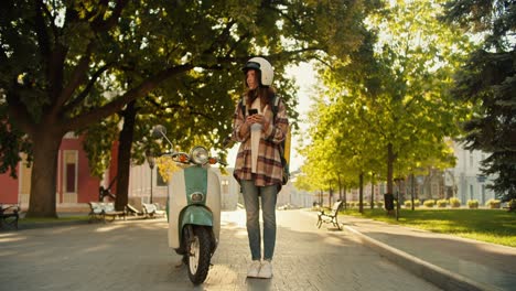 the courier girl came to deliver the order and looks around looking at the map on her phone and looking in different directions to understand where she should go next on her moped in the summer