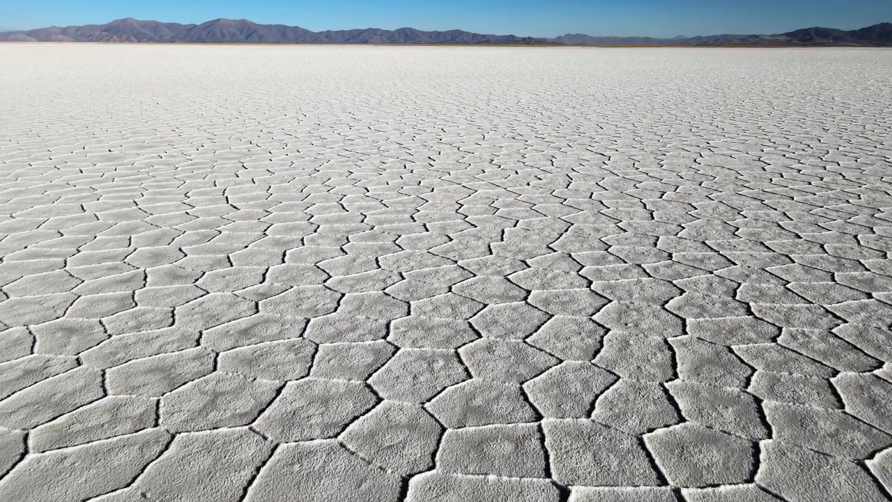 Ampia veduta della distesa salina di Salinas Grandes con motivi poligonali secchi che si estendono verso montagne lontane sotto un cielo azzurro limpido, utile come paesaggio astratto o riprese di repertorio sul cambiamento climatico
