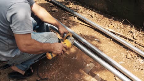 man cutting a galvanized steel tube with an industrial electric angle grinder to elaborate a metal structure in a rural environment construction site worplace