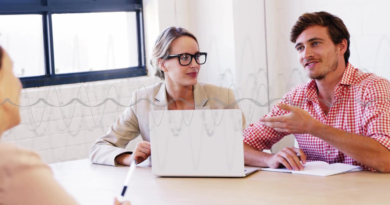 Uomo che chiarisce un punto dopo che il collega a sinistra ha indicato con la penna, donna che annuisce vicino al laptop durante una riunione di lavoro.
