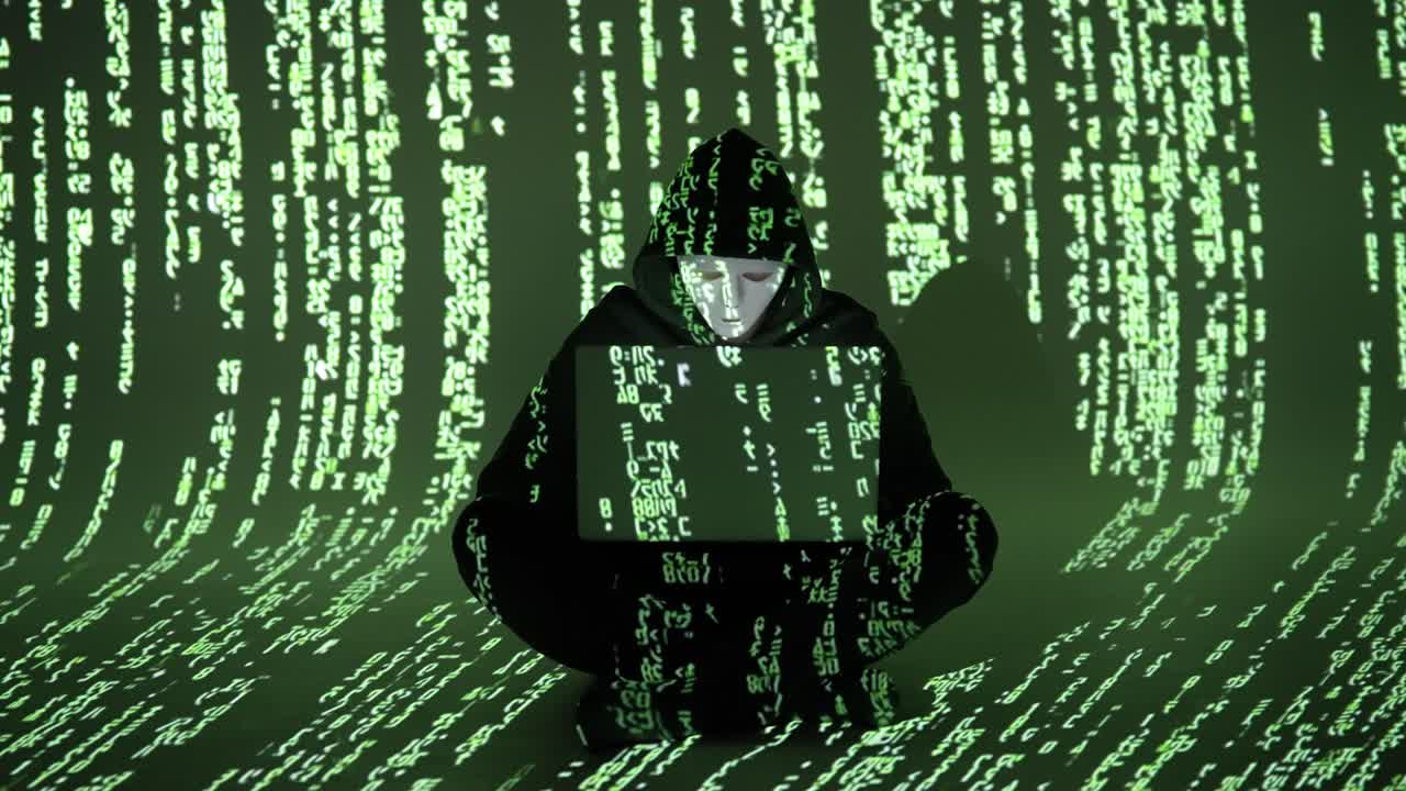 A masked cybercriminal sits cross-legged with a laptop as green matrix-like code falls around. The scene conveys cybercrime, digital infiltration, and anonymous activity in the dark web realm
