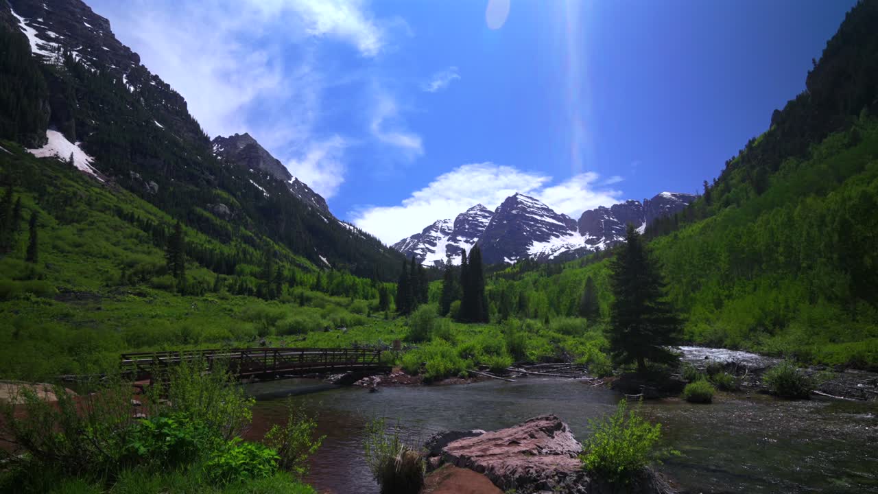 Maroon creek pedestrian walking bridge river Crater lake trail Maroon Bells Pyramid Peak 14er Wilderness morning sunny blue sky Aspen Snowmass Colorado Elk Mountains Range White River Forest pan down