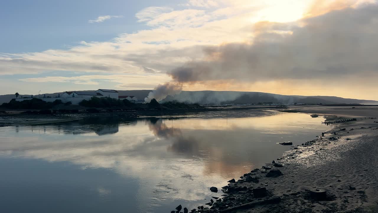 plano general de una quema controlada en un campo rural, con el tenue perfil de una ciudad distante visible en el horizonte bajo un día despejado