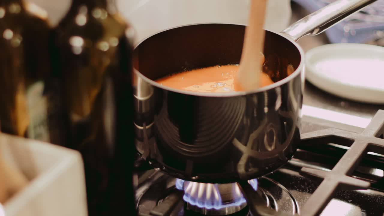 Creamy tomato soup simmering on a gas stove, stirred with a wooden spoon.